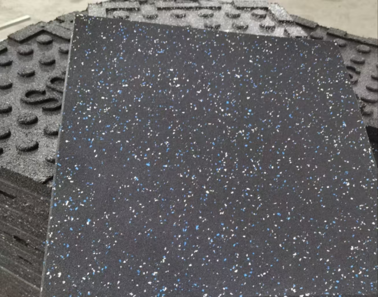 Close-up of a black rubber mat with blue and white speckles and a textured edge.